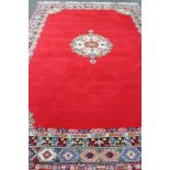 A fringed woolen Persian carpet on red ground with central medallion 440 cm x 295 cm.