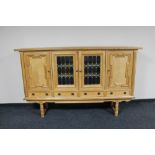 A blonde oak four door sideboard on raised legs