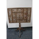 A carved fret work fire screen on tripod base