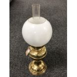 A brass oil lamp with glass chimney and opaque glass shade