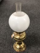 A brass oil lamp with glass chimney and opaque glass shade