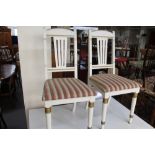 A pair of white and gilded dining room chairs.