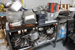 A two tier metal stand containing a large quantity of stainless cooking items and a further metal