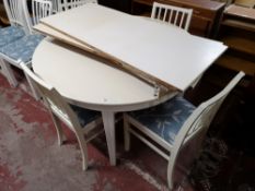 A painted white extending dining table, with three leaves and four dining chairs.