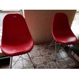 A pair of red contemporary chairs with metal under stretchers.