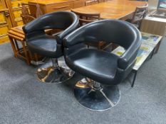 A pair of black leather swivel gas lift salon chairs on chrome bases