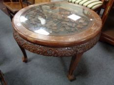 A circular heavily carved oriental style coffee table with glass top
