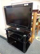 A Philips 32" LCD TV with remote on black glass three tier stand