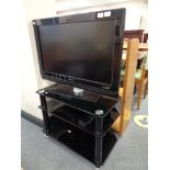 A Philips 32" LCD TV with remote on black glass three tier stand