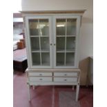 A cream and gilt double door display cabinet fitted with four drawers