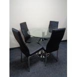 A circular glass topped pedestal table and four black leather dining chairs on metal legs
