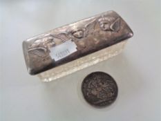 A silver topped dressing table pot depicting three cherubs together with an 1899 Victoria coin