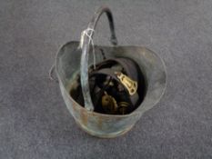 An antique copper coal bucket containing horse brasses on leather straps