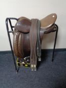 A leather saddle on metal stand with a box of leather tack and stirrups