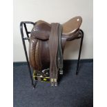 A leather saddle on metal stand with a box of leather tack and stirrups