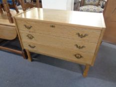 A blonde oak three drawer chest with brass drop handles