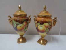 A pair of Coalport porcelain urn shaped lidded vases painted with panels of fruit by M.