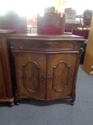 An antique mahogany serpentine fronted cabinet fitted a drawer