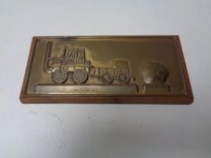 A copper embossed plaque of a steam train mounted on board