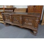 A 20th century heavily carved oak triple door sideboard with frieze panelled doors