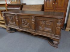 A 20th century heavily carved oak triple door sideboard with frieze panelled doors