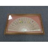 A vintage hand fan depicting flowers and butterflies in a display frame