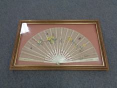 A vintage hand fan depicting flowers and butterflies in a display frame