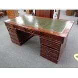 A mahogany twin pedestal ten drawer desk with a green tooled leather inset panel