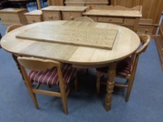 A circular blonde oak table with two leaves and four elbow chairs