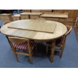 A circular blonde oak table with two leaves and four elbow chairs