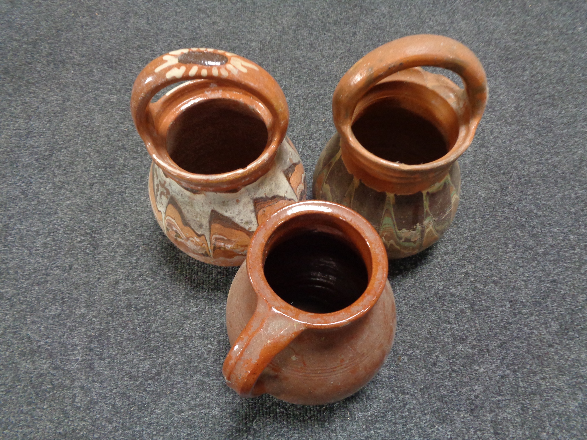 A glazed earthenware jug together with two further pottery vases with handles