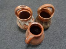 A glazed earthenware jug together with two further pottery vases with handles