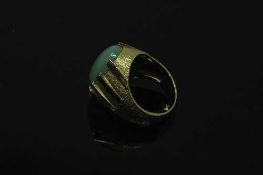 A continental yellow gold ring, the textured shank set with a cabochon apple green jade stone,