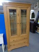 A contemporary oak double door glazed cabinet fitted with two drawers