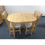 An oval rubber wood extending dining table fitted with a leaf together with two rail backed chairs