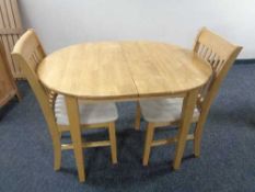 An oval rubber wood extending dining table fitted with a leaf together with two rail backed chairs