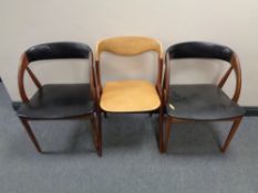 A pair of mid century Danish teak armchairs upholstered in black vinyl together with one other