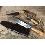 Three wooden handled hunting knives in leather sheaths.