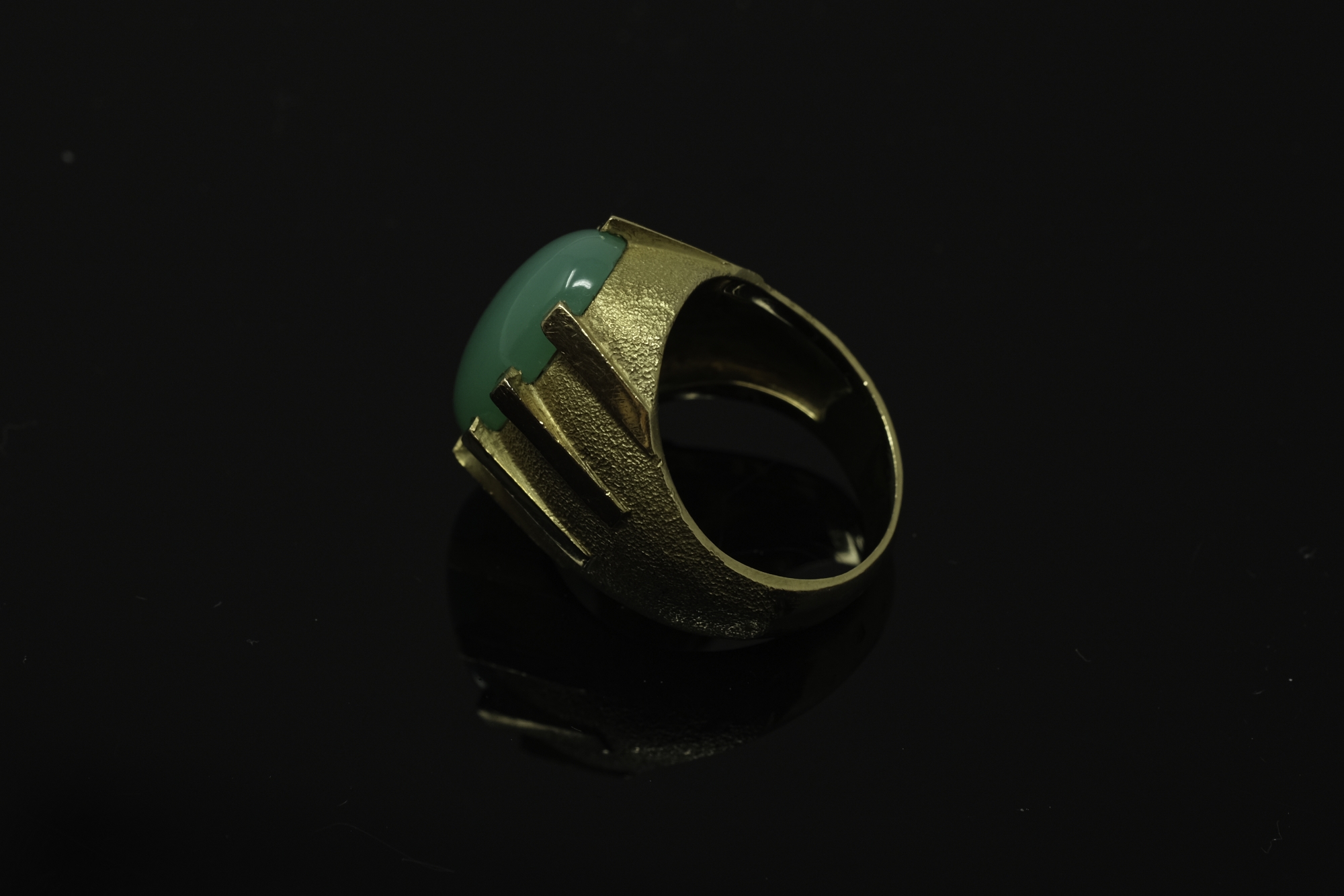 A continental yellow gold ring, the textured shank set with a cabochon apple green jade stone,