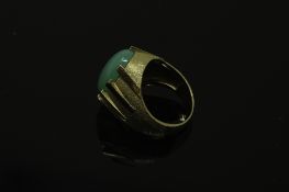 A continental yellow gold ring, the textured shank set with a cabochon apple green jade stone,