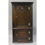 A George III provincial oak floor standing corner cabinet, the moulded pediment above two panelled