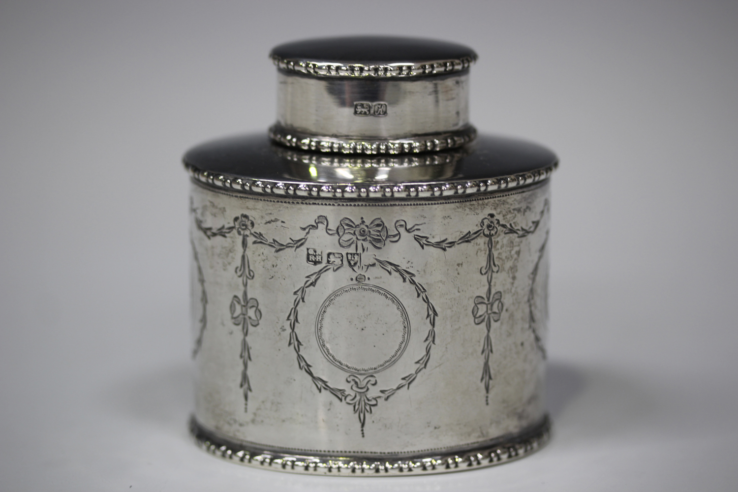 A George V silver oval tea caddy, engraved with opposing bellflower pendant cartouche and bellflower
