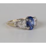 A gold, sapphire and diamond ring, claw set with an oval cut sapphire between circular cut diamond