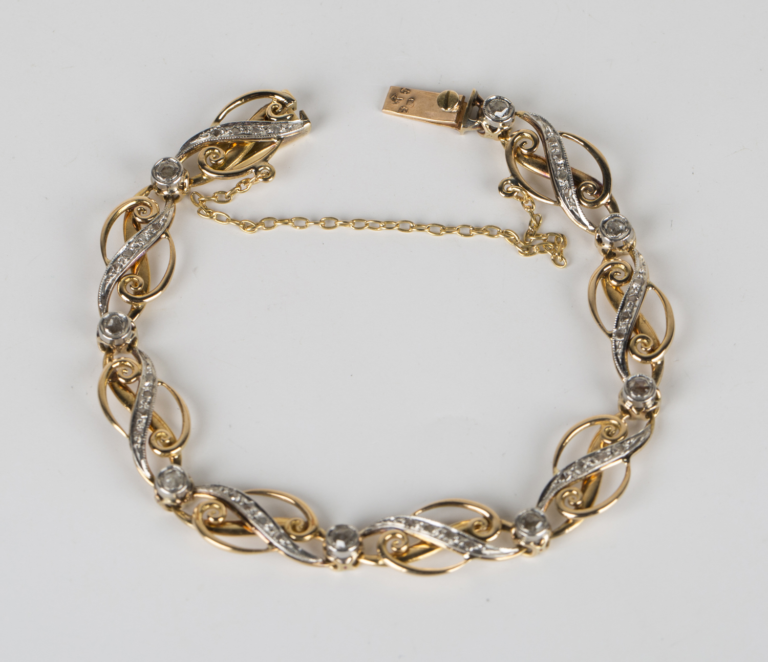 A French two colour gold and diamond bracelet, each link in a scrolling design, mounted with rose