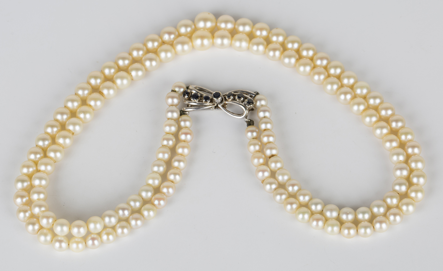 A three row necklace of graduated cultured pearls on a white gold and sapphire clasp, designed as