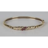 A 9ct gold, ruby and diamond oval hinged bangle, claw set with a row of three circular cut rubies