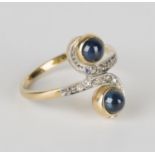 A gold, cabochon sapphire and diamond twin cluster ring in a scrolling crossover design, mounted
