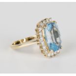 An 18ct gold, blue topaz and diamond ring, claw set with an oval cut blue topaz within a surround of