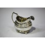 A George III silver cream jug of cushion form with gadrooned rim and beaded handle, raised on ball