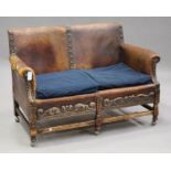 An early 20th century Jacobean Revival oak and brown leather two-seat settee with carved and brass